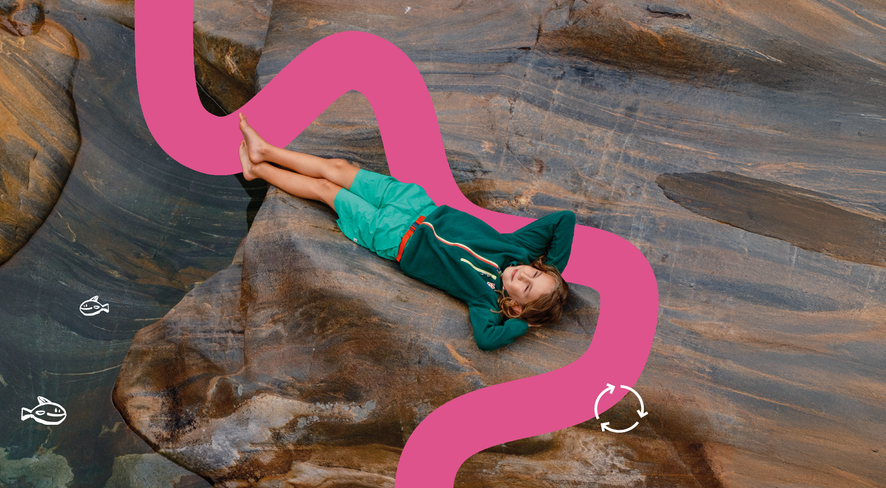 Kind liegt entspannt auf einem Felsen am Wasser