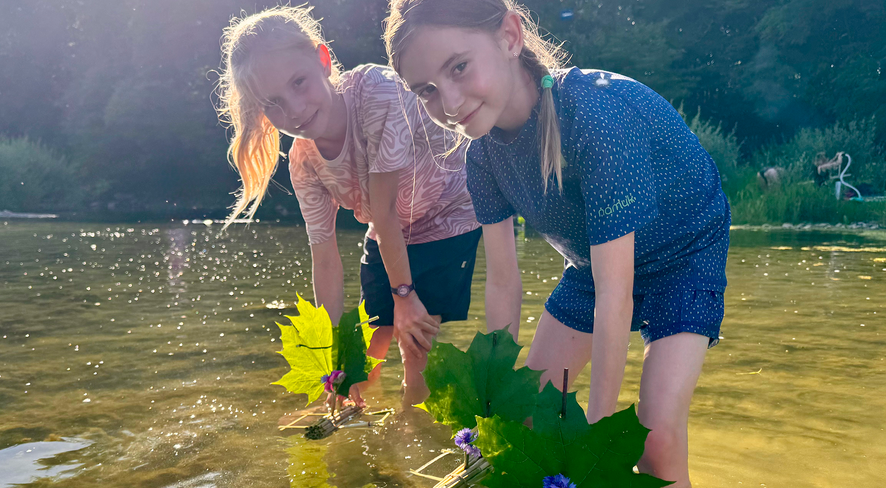 Zwei Mädchen stehen im Wasser mit ihren verzierten Schilfbooten