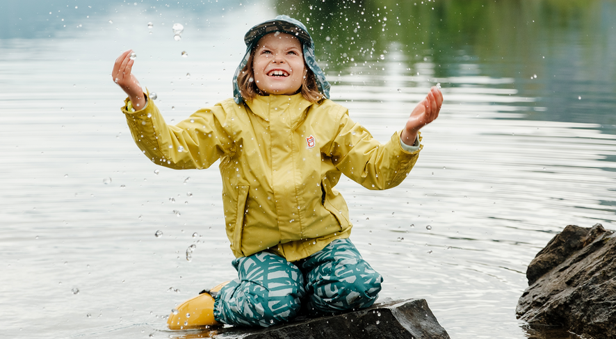 Kind mit Regenbekleidung spielt im Wasser