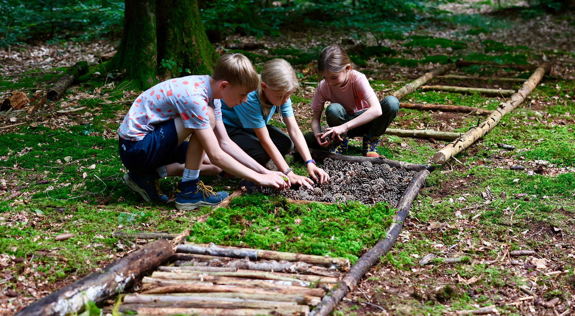  Drei Kinder legen gemeinsam einen Barfusspfad auf den Waldboden